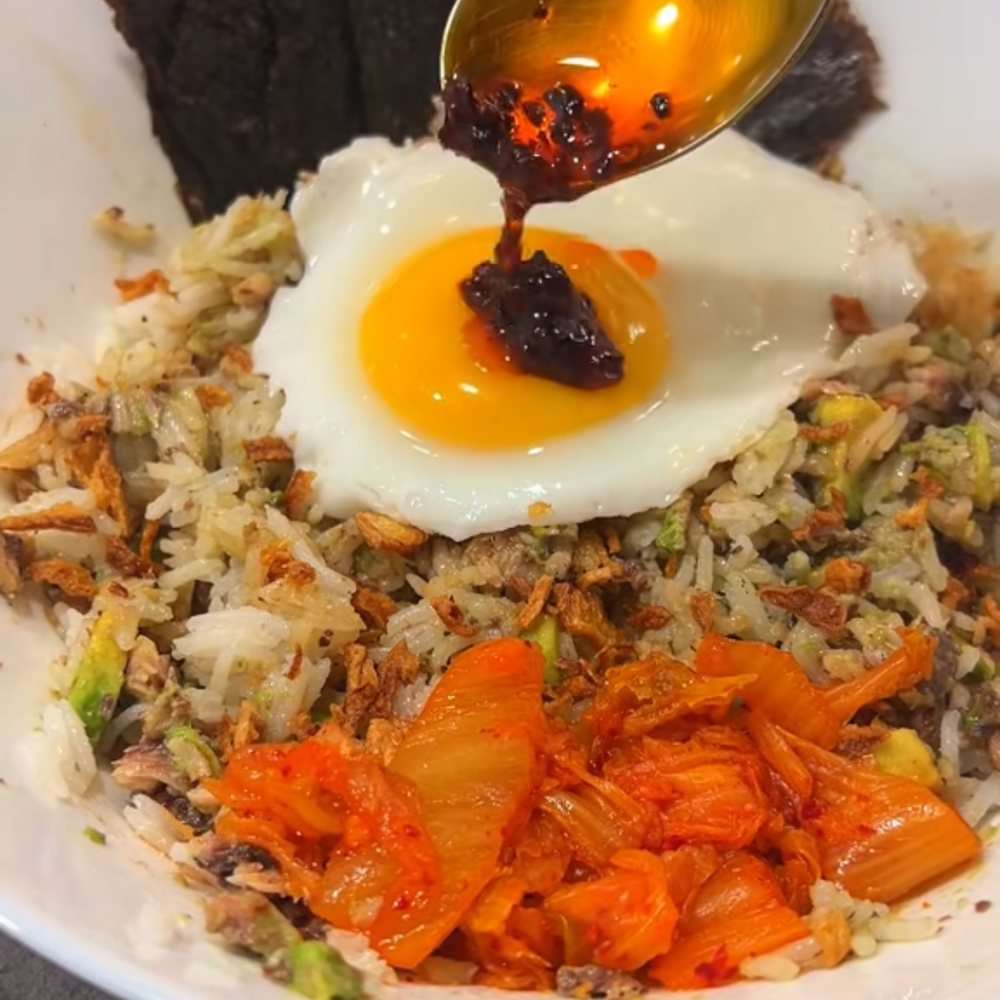 Sardine rice bowl with a fried egg, kimchi and crispy onions, chilli oil being spooned over the yolk