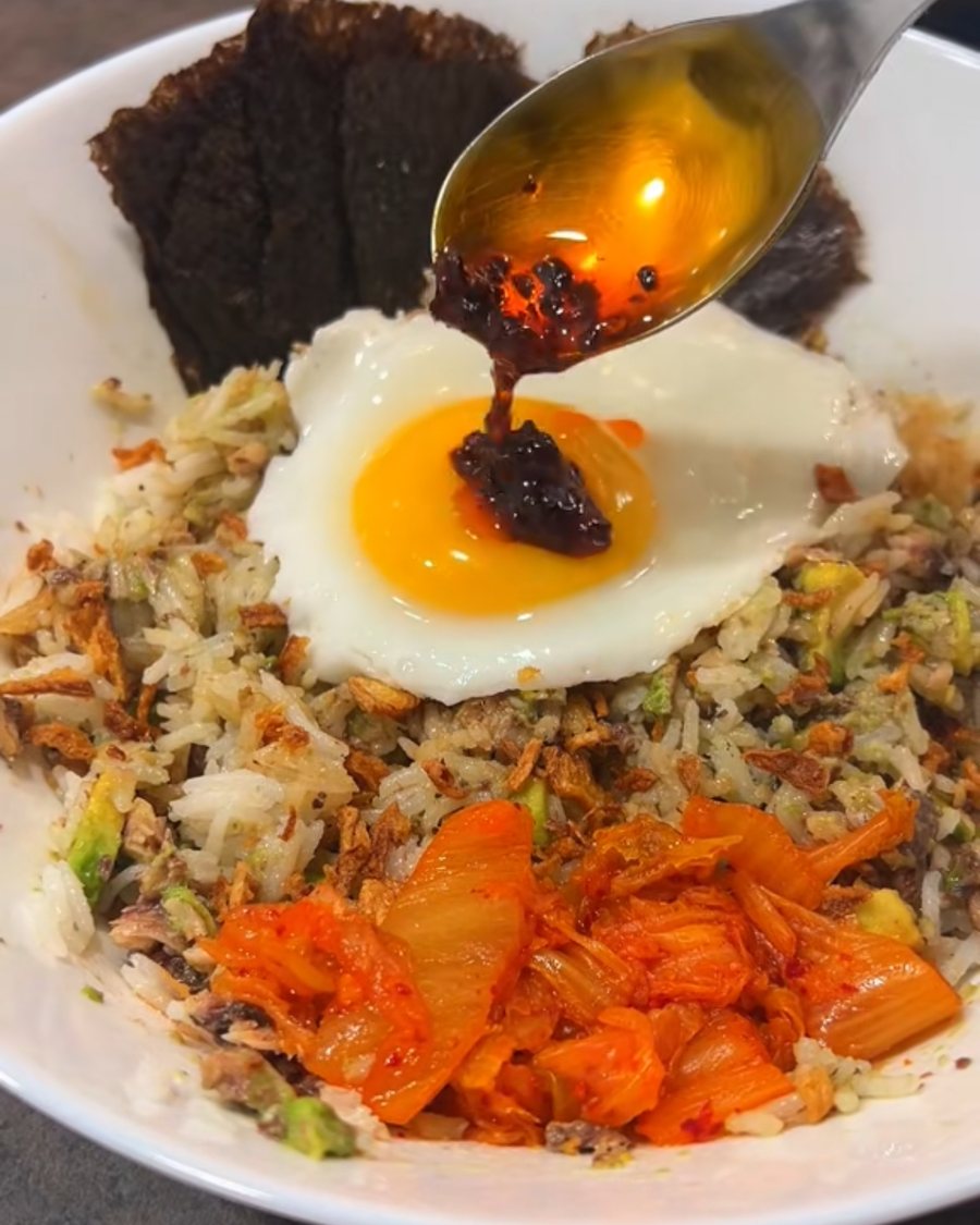 Sardine rice bowl topped with a fried egg, kimchi and crispy onions, chilli oil spooned over the yolk