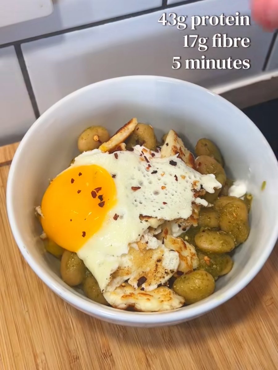 Pesto butter beans in a bowl topped with seared halloumi, a fried egg and chilli flakes