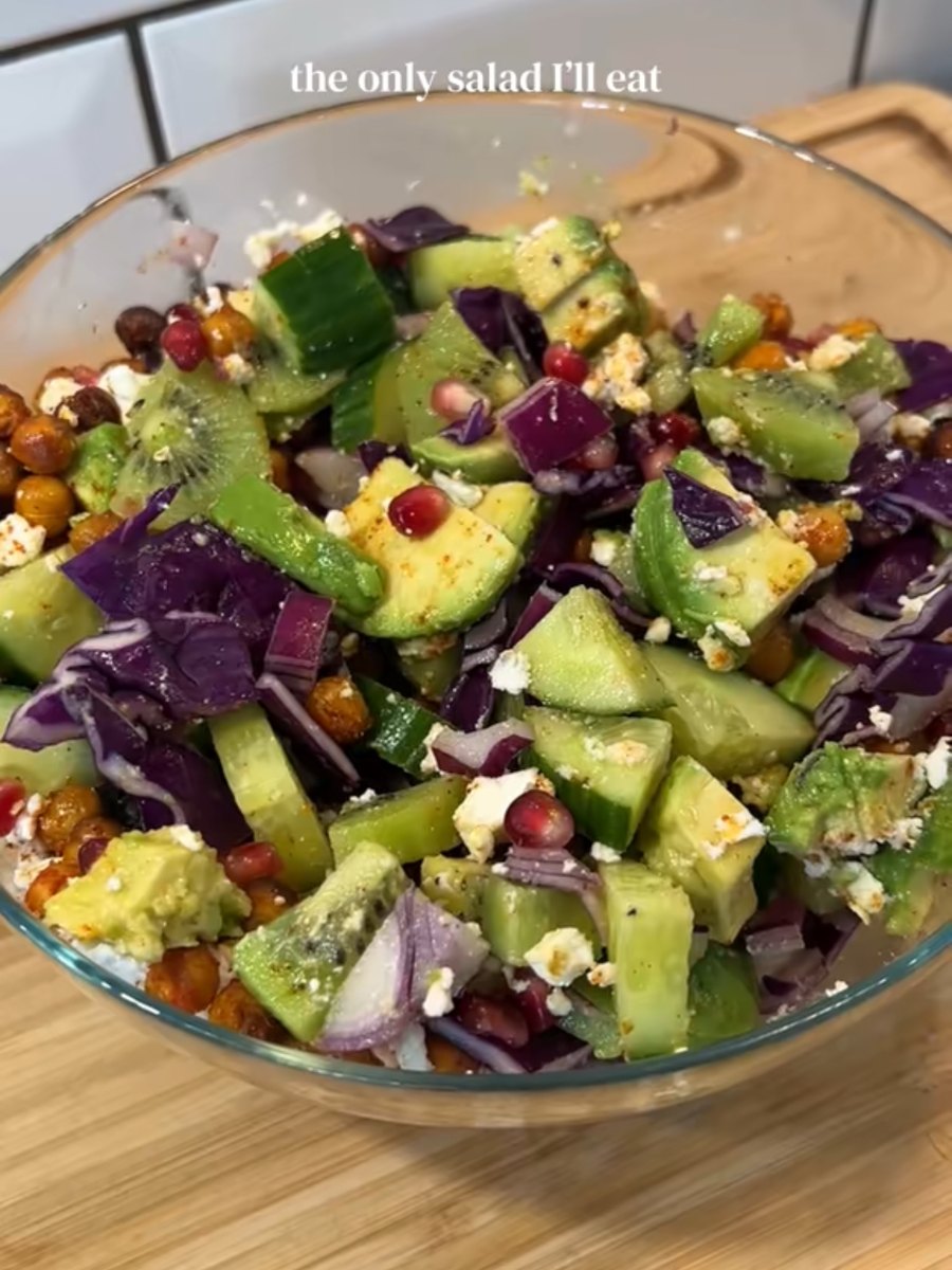 Glass bowl of red cabbage, cucumber, avocado, kiwi, pomegranate, roasted chickpeas and crumbled feta