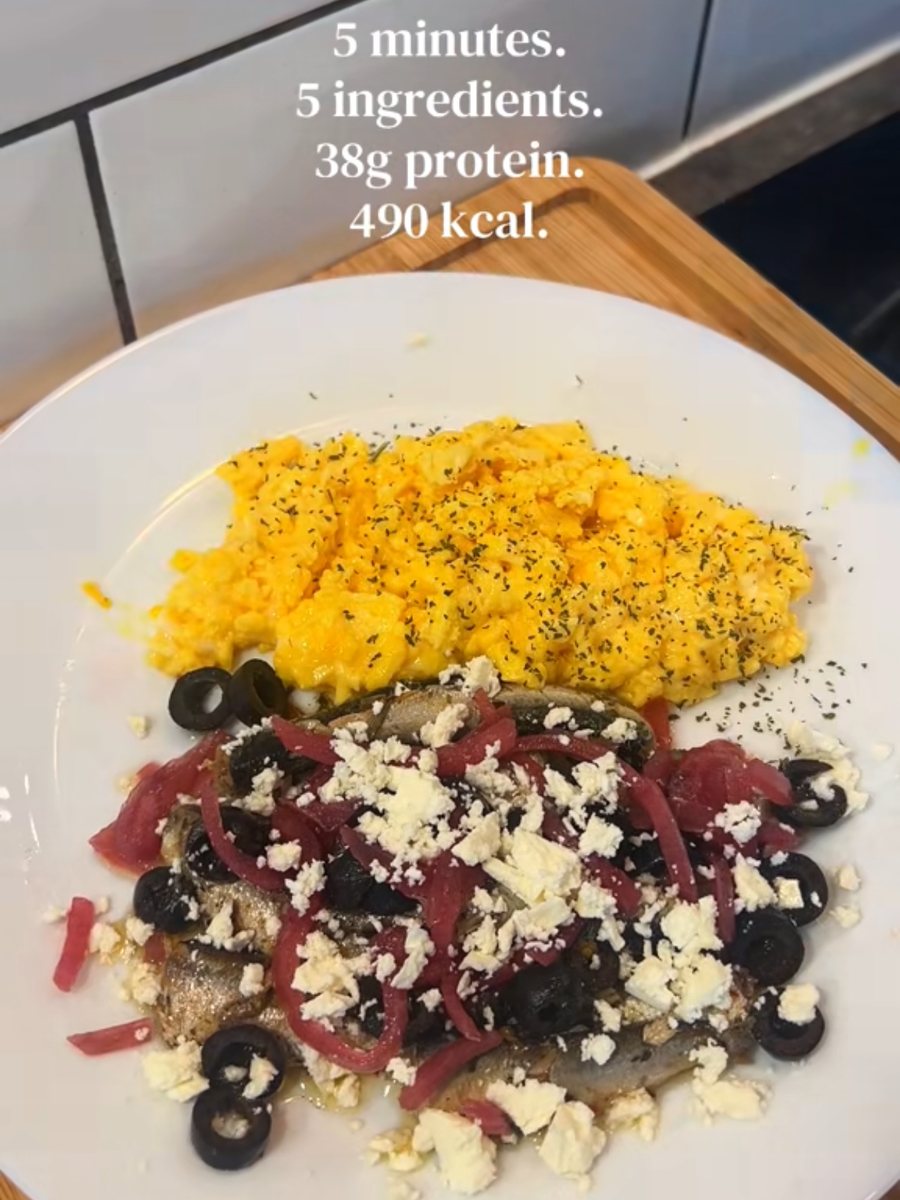 Soft scrambled eggs beside sardines topped with feta, black olives and pickled red onions